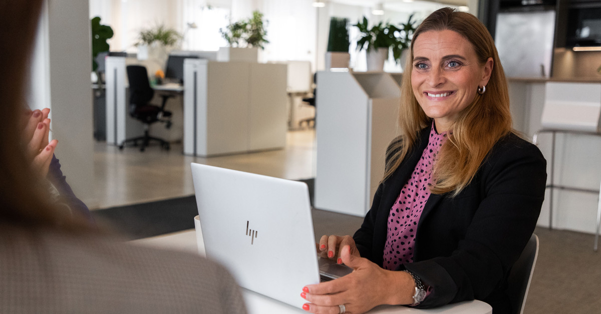 En kvinnlig medarbetare från SJR möter en kollega i ett öppet kontor och diskuterar lösningar inom rekrytering, bemanning och interim management, där erfarenhet, ledarskap och samarbete är i fokus.