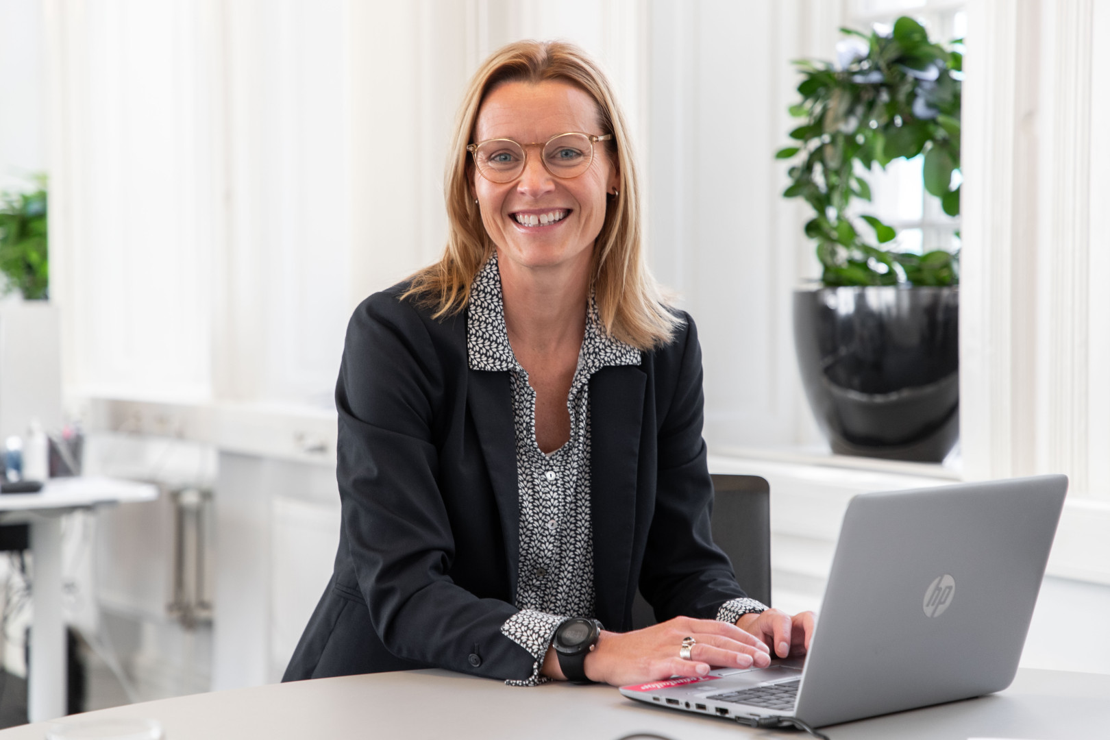 En kvinnlig medarbetare från SJR arbetar vid en laptop i ett ljust och luftigt kontor med gröna växter i bakgrunden – en miljö som främjar hållbart arbetsklimat.