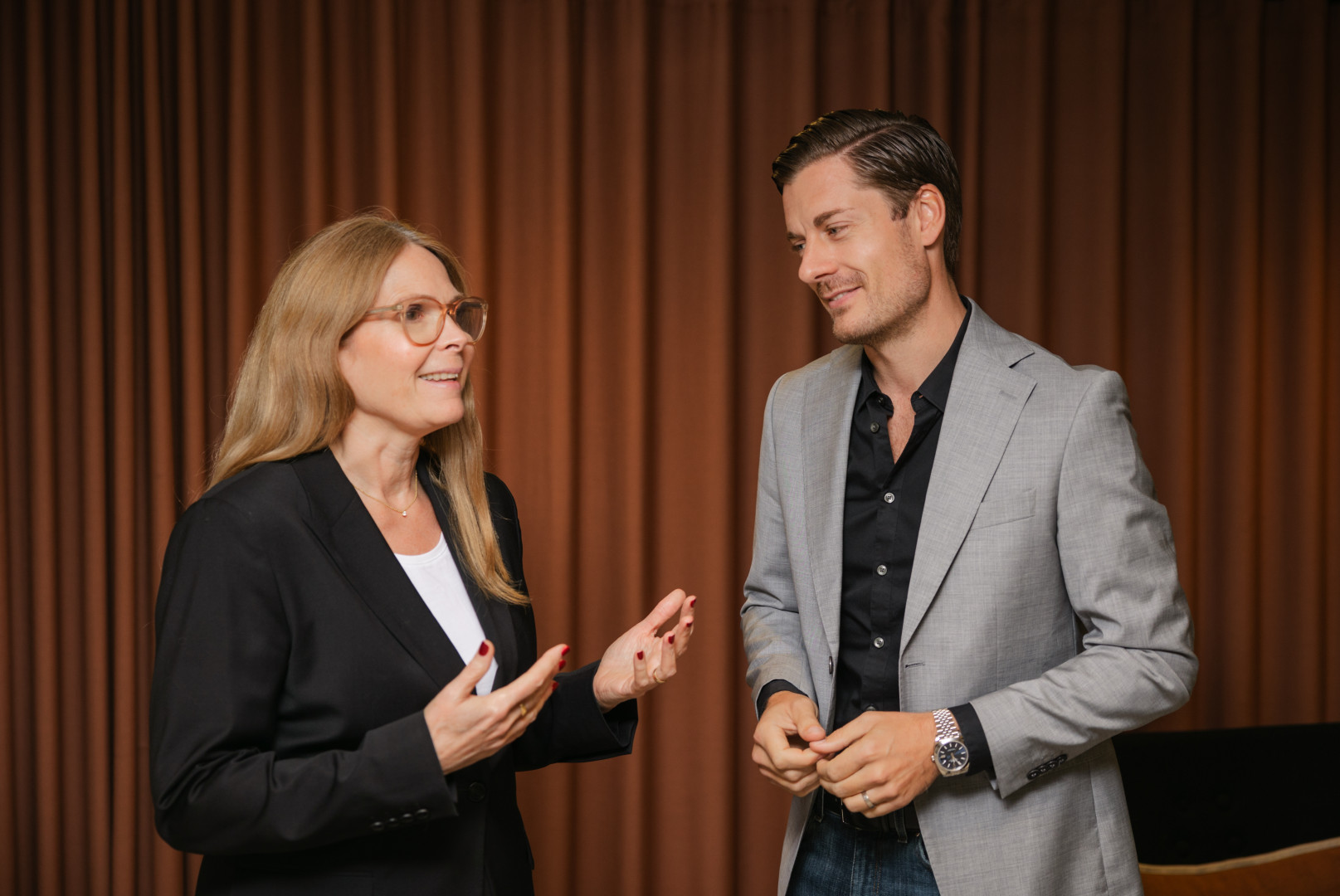 Två kollegor från SJR samtalar framför en brun gardin, där samarbetet mellan kompetensområden tydligt genomsyrar dialogen.