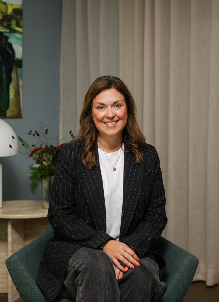 En kvinnlig konsultchef från SJR sitter leende i en modern fåtölj med konst och växter i bakgrunden, vilket skapar en varm och inbjudande stämning.