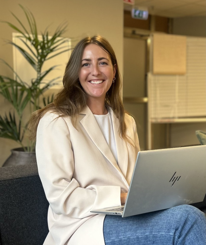 Sofia Erikson, en medarbetare från SJR i Göteborg, sitter avslappnat i en kontorssoffa med en laptop i knät och ett välkomnande leende – redo att stötta kunder med rekrytering och konsultlösningar inom ekonomi, finans och HR.