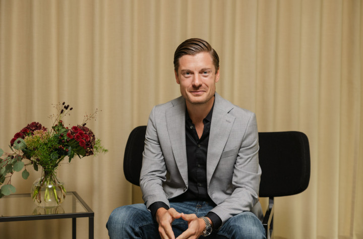 En manlig medarbetare från SJR sitter framför en bukett med höstfärger, vilket skapar en mjuk kontrast till hans affärslook och bidrar till en inbjudande stämning.