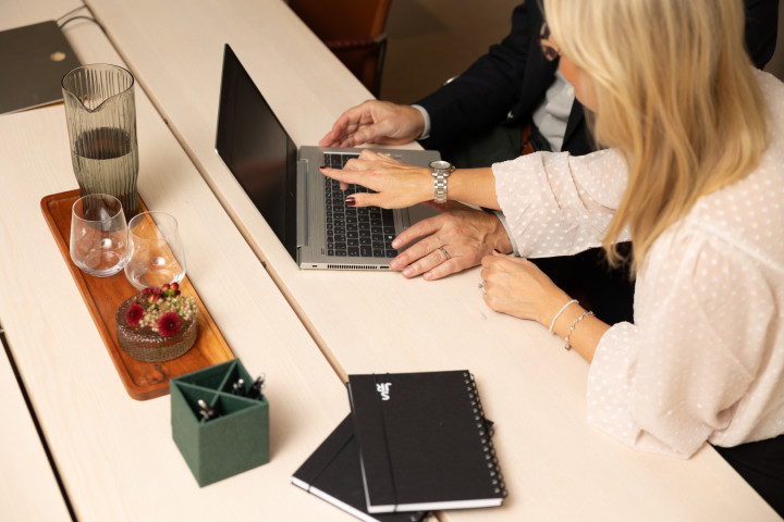 Två medarbetare tittar på en laptop och diskuterar kompetensbehov och profiler i ett modern och varmt konferensrum.