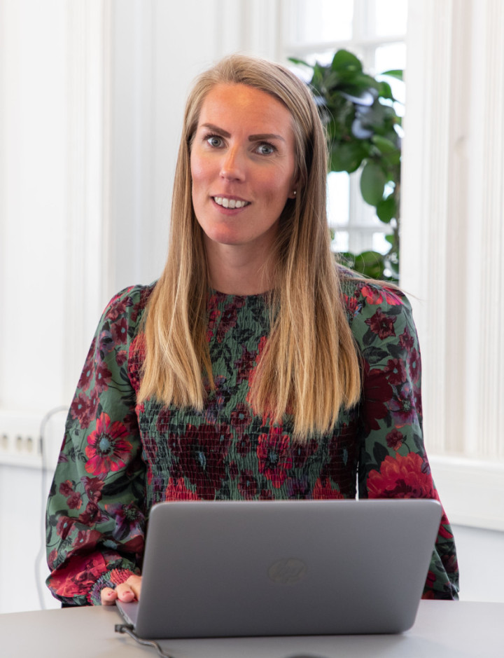 En leende kvinnlig kollega från SJR som sitter vid ett bord med sin laptop och utstrålar professionalism och förtroendefulla relationer.