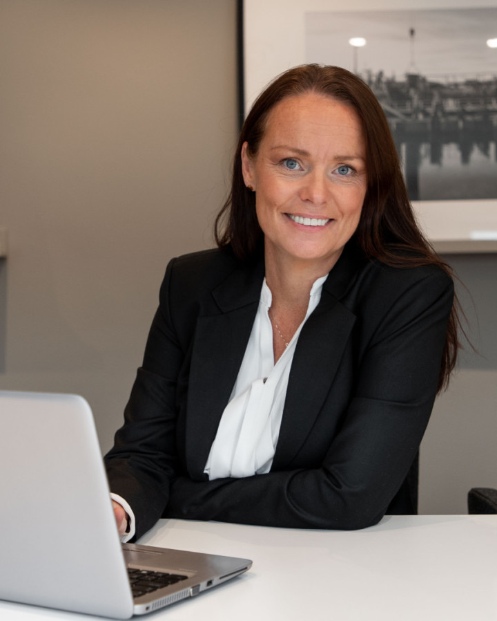 En leende kvinnlig kollega från SJR som sitter vid ett bord med sin laptop, klädd i kavaj och utstrålar professionalism och förtroendefulla relationer.